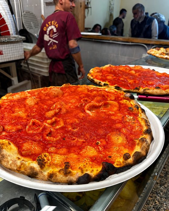 Pizze rosse appena sfornate sul banco, il pizzaiolo al lavoro