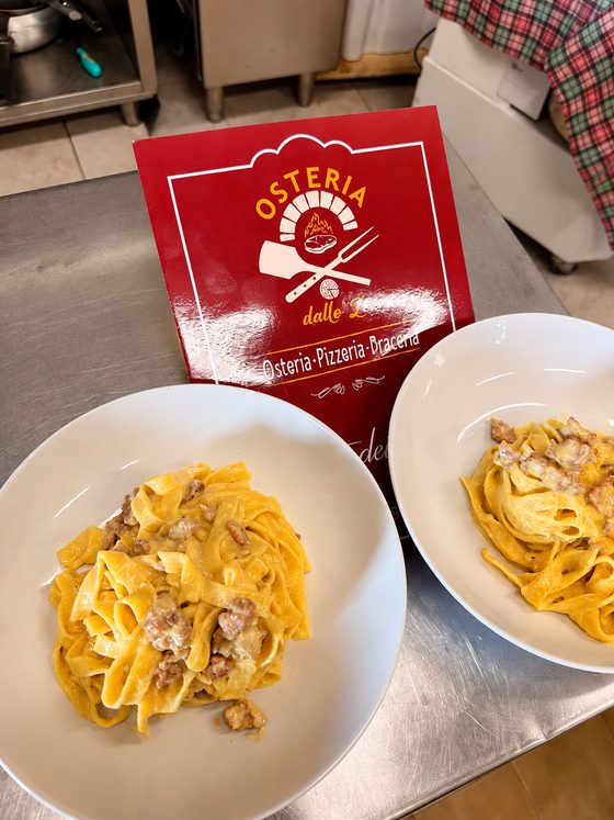 Due piatti di fettuccine col guanciale davanti al menu dell'osteria