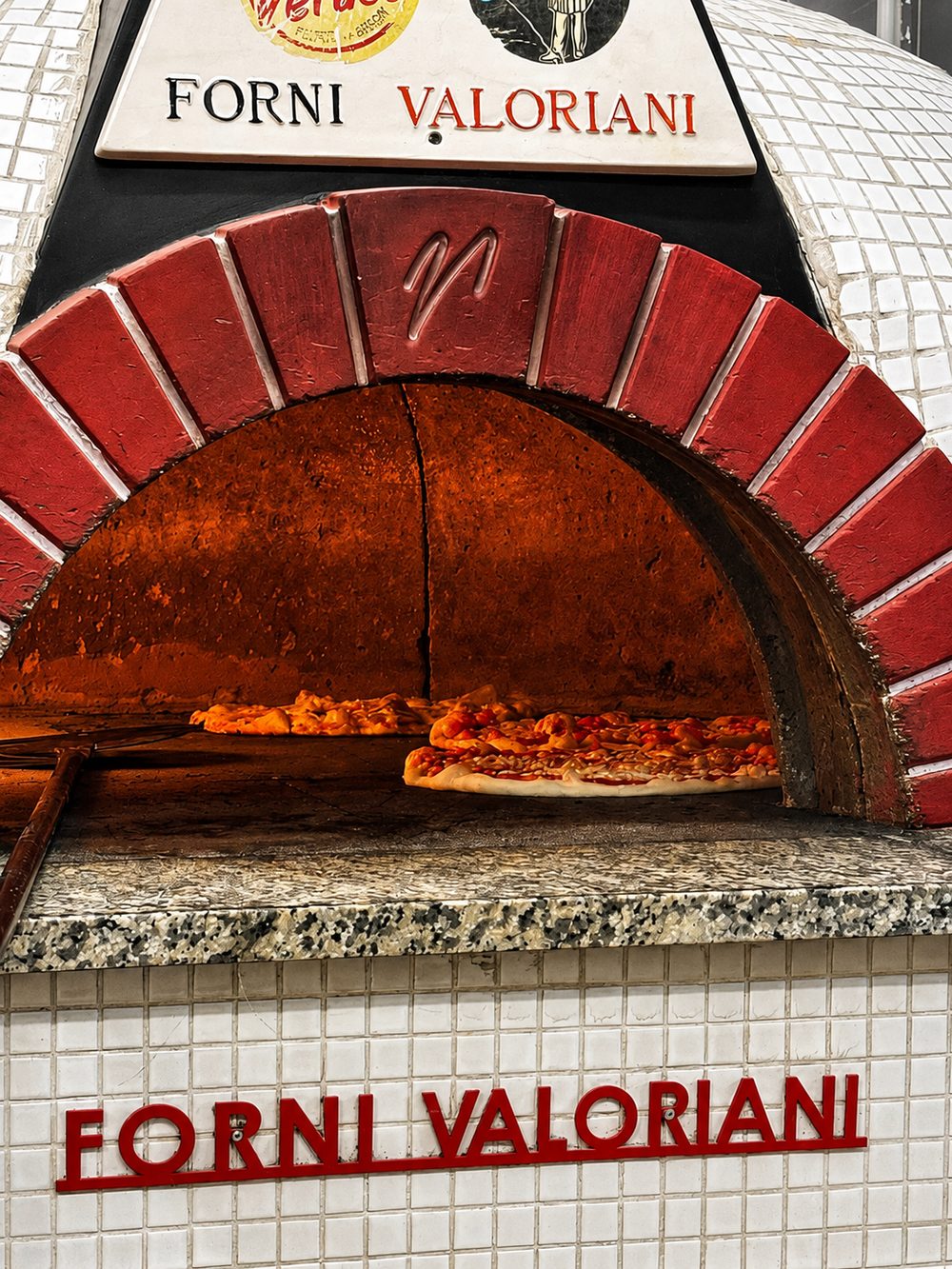 Il forno a legna Valoriani con le pizze in cottura sotto l'arco di mattoni rossi