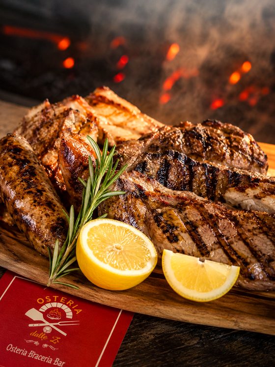 Tagliere di grigliata mista con rosmarino e limone, le braci accese sullo sfondo
