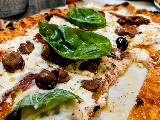 Dettaglio di pizza con olive, alici, stracciatella e basilico