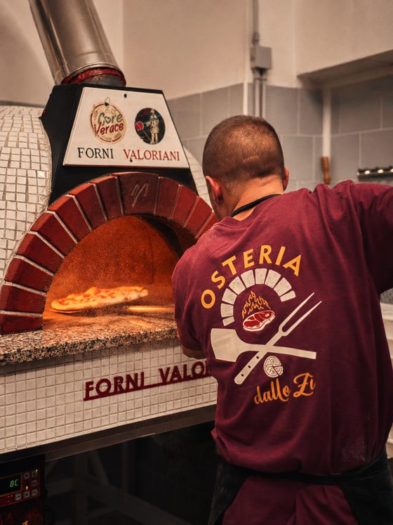 La pizza che scivola dalla pala verso il piano del forno, con la semola nell'aria