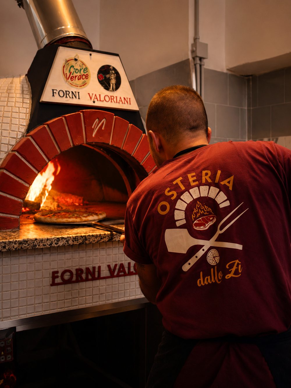 Il pizzaiolo dell'Osteria dallo Zì mette in forno una pizza, con la fiamma viva nel Valoriani