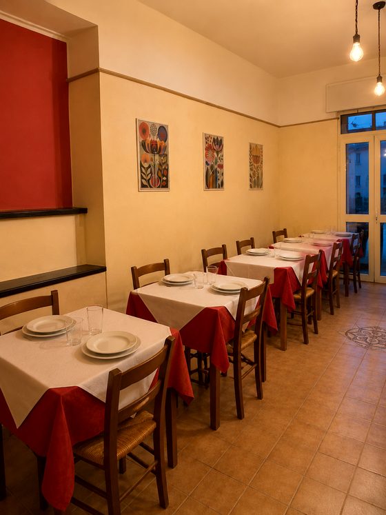 La sala dell'osteria apparecchiata all'ora blu, con le tovaglie rosse e le luci calde