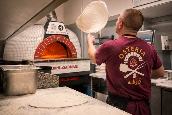 Il pizzaiolo lancia il disco di pasta in aria davanti al forno acceso